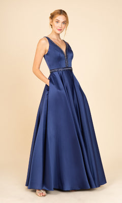 A woman models the Beaded-Waist Long Satin Prom Dress: Eureka 9010 in navy, featuring a sleeveless A-line silhouette with a deep V-neckline and beaded waist, standing against a plain beige background.