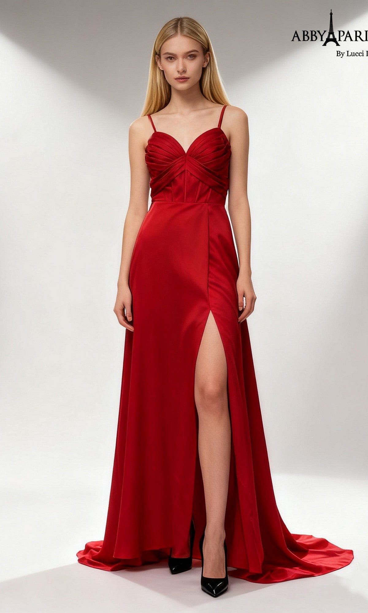 A woman in the Abby Paris 90386 long prom dress in wine, featuring a sleeveless satin design and thigh-high slit, pairs it with black high heels and stands against a plain, light background.