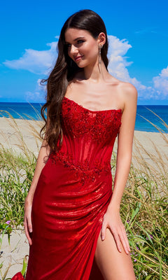A woman in the Amelia Couture 9055 Strapless Long Prom Dress stands on a sandy beach, surrounded by tall grass with the blue sky and shimmering ocean in the background.