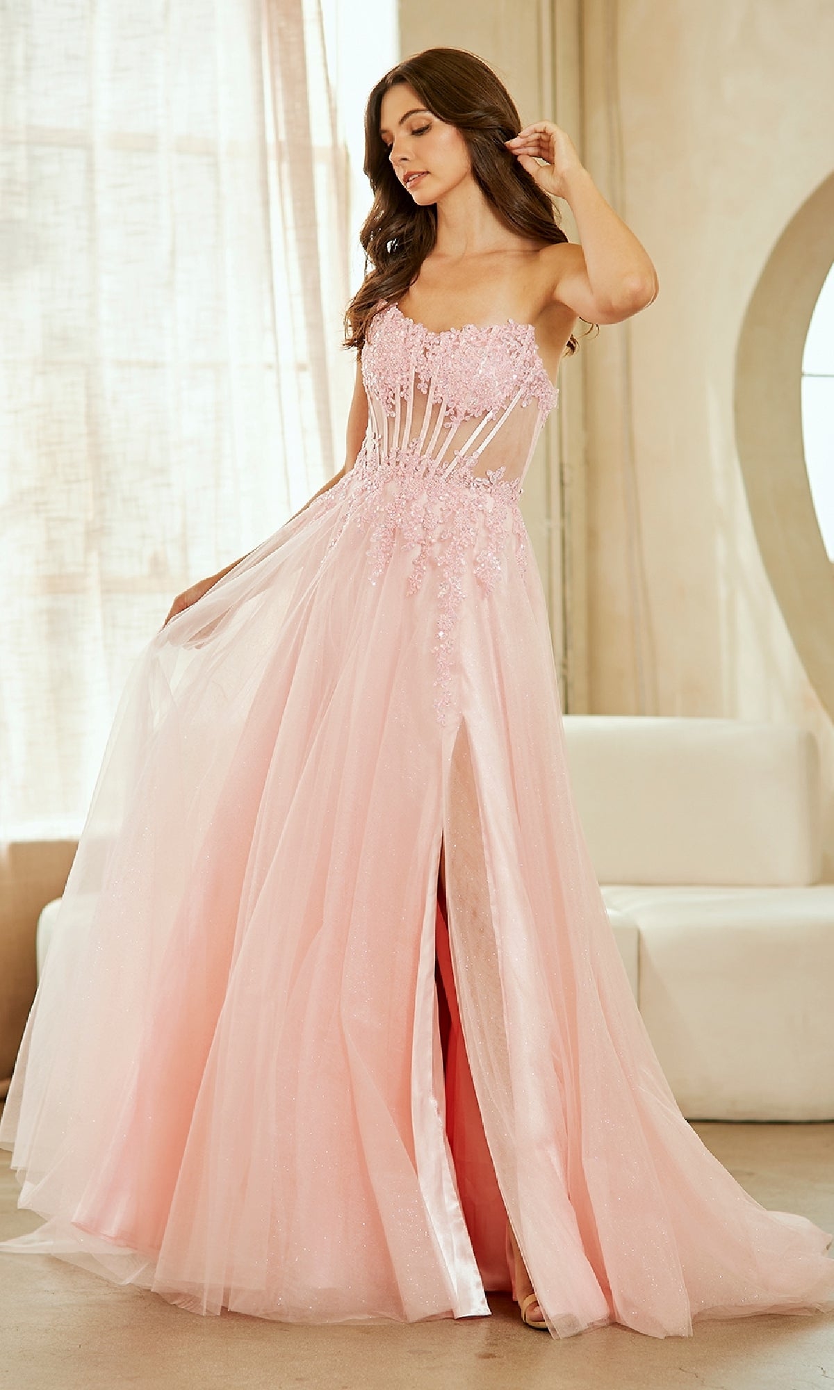 Woman wearing a pink evening gown with a high slit in a room with curtains and a mirror.