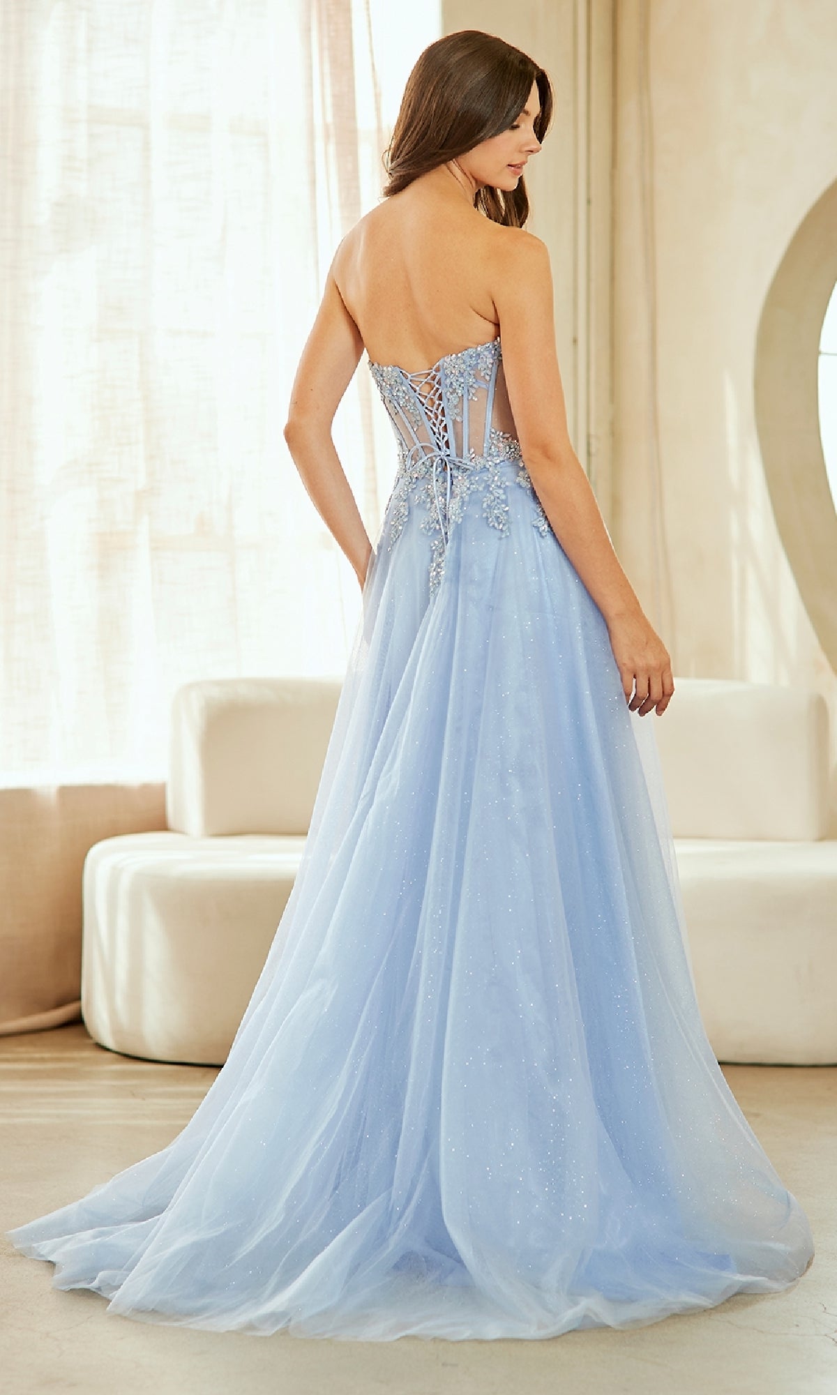 Woman modeling the back of a light blue evening gown with a corset bodice in an indoor setting.
