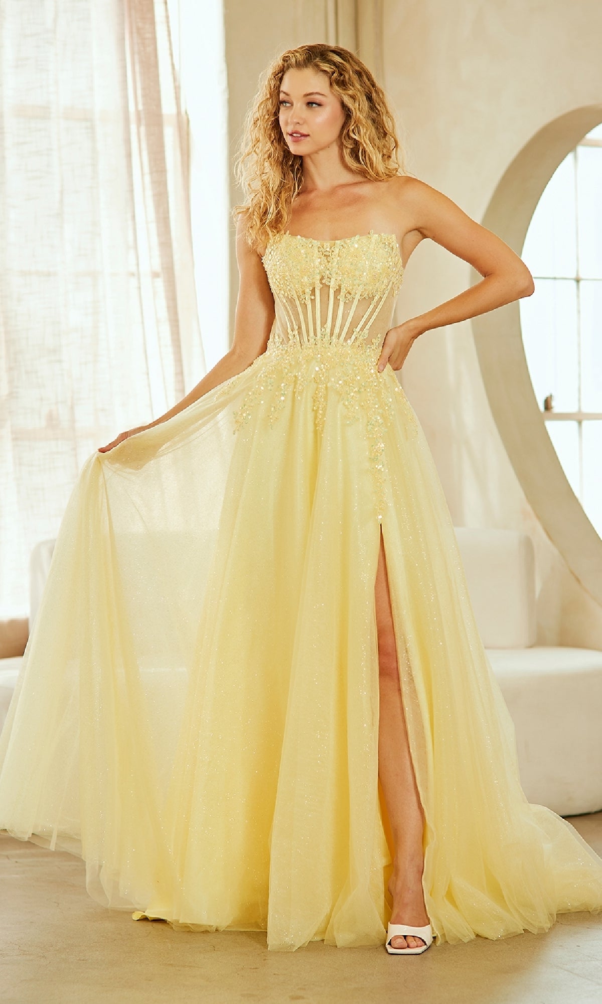 Woman wearing a strapless yellow evening gown standing in a well lit room.