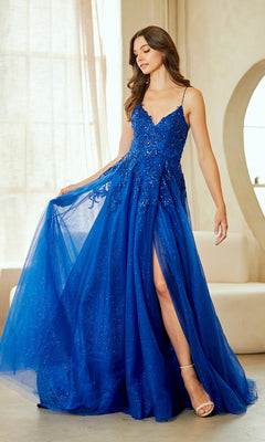 A woman in a vibrant blue, floor-length Lace-Up Long Prom Ball Gown: Amelia Couture 9079 with thin straps and a slit stands indoors holding out part of the skirt.