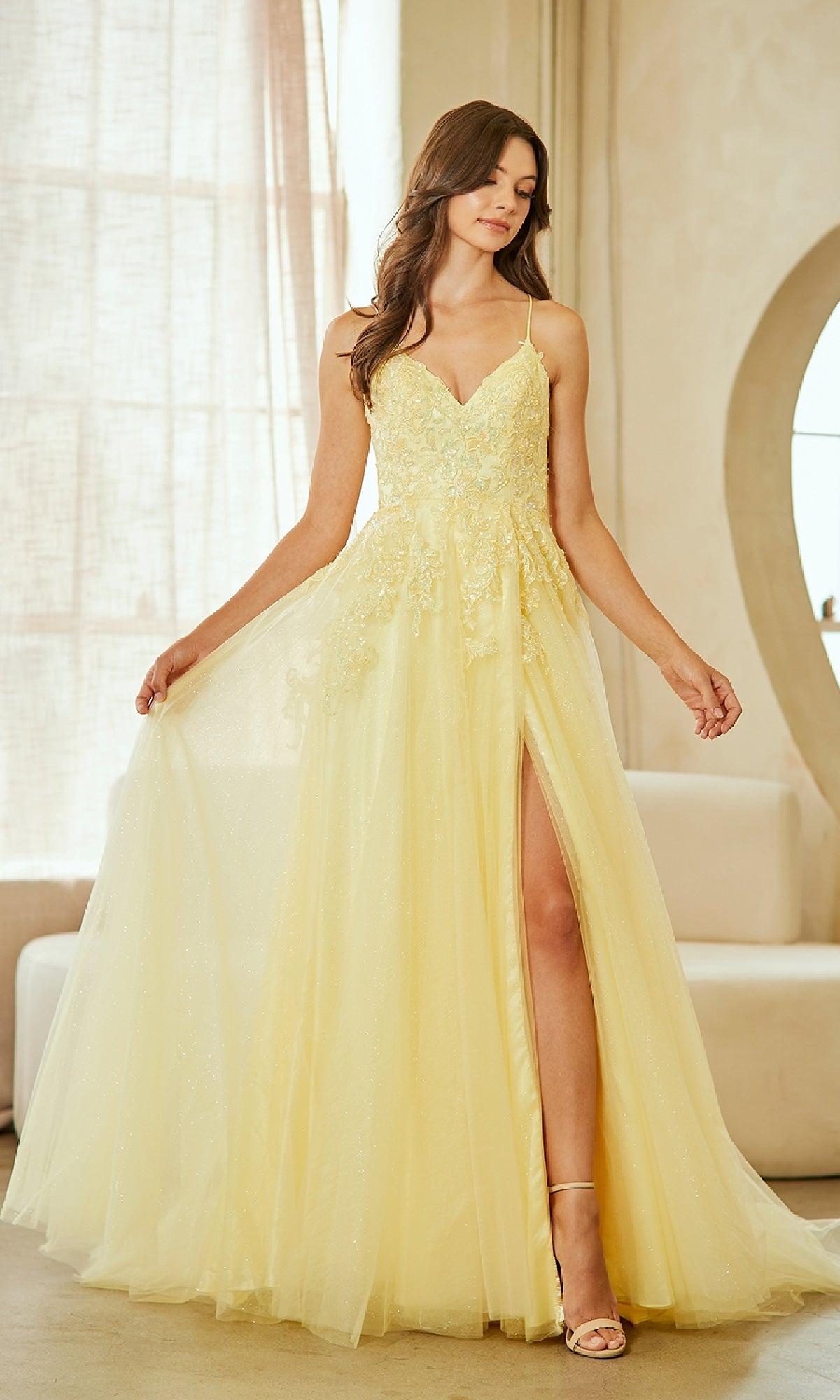 Woman wearing a yellow evening gown with a high slit in a softly lit room.