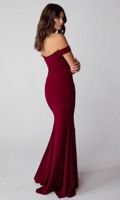 A woman wearing the Off-Shoulder Long Jersey Prom Dress Eureka 9081, featuring a fitted mermaid skirt, poses turned to the side against a plain light background.