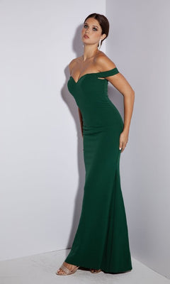 A woman models the Eureka 9081 Off-Shoulder Long Jersey Prom Dress with a mermaid skirt, pairing it with strappy high-heeled sandals and drop earrings as she poses against a plain white wall.