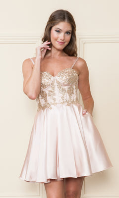 A woman stands against a light wall wearing the Corset-Style Strapless Short Homecoming Dress 9084, a light pink cocktail dress with gold floral embroidery and a beaded corset bodice.