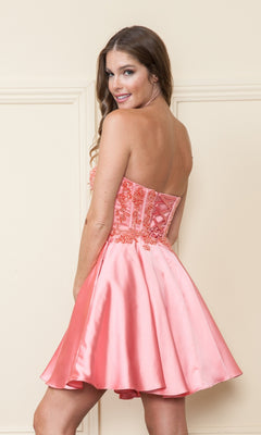 Woman in the Corset-Style Strapless Short Homecoming Dress 9084—pink satin with floral embroidery and a beaded corset bodice—stands indoors, looking over her shoulder at the camera.