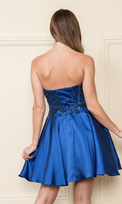 A woman with long hair faces away, wearing the Corset-Style Strapless Short Homecoming Dress 9084 in royal blue with a beaded corset bodice, lace-up back, and embroidered details.