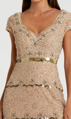 A woman in the Mac Duggal 9089 cap-sleeve beaded formal dress, light beige with gold trim and intricate bead and sequin floral embellishments.