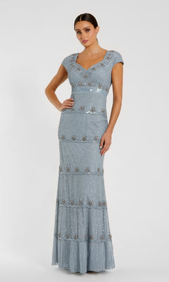 A woman wears the Mac Duggal 9089 Cap-Sleeve Beaded Formal Dress, a floor-length light blue gown adorned with sequins and beads, set against a plain white background.