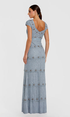 A woman models the Mac Duggal 9089 Cap-Sleeve Beaded Formal Dress in light blue, featuring beaded embellishments and a deep V-back, standing against a plain background.