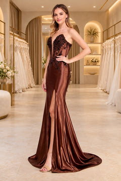 A woman wearing an Amelia Couture 9107 brown strapless sweetheart prom dress featuring a sheer, beaded bodice, sequin appliques, and a high leg slit.