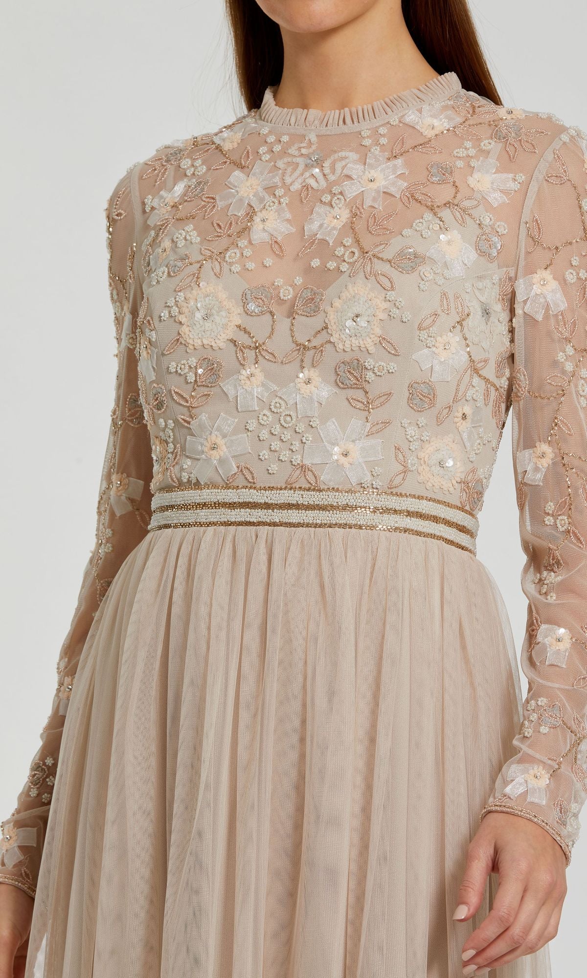 A person wearing the Long Sleeve Vanilla Formal Gown by Mac Duggal 9132—a beige A-line dress featuring floral embroidery and pearl-adorned bodice, with a mesh skirt.