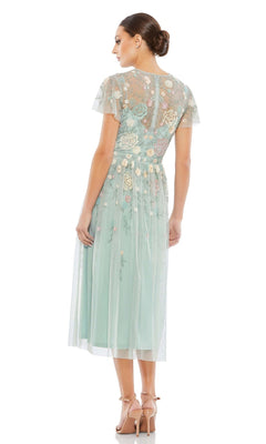 A woman faces away wearing the Mac Duggal Knee Length Wedding Guest Dress 9134, a light blue A-line dress with short sleeves and floral embroidery. She pairs it with nude heels and a low bun. Set against a white background.