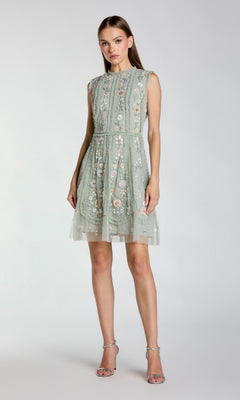 A woman wears the Mac Duggal 9135 Embroidered Short Party Dress in light green, featuring floral details, posed against a plain background and styled with strappy high-heeled sandals.