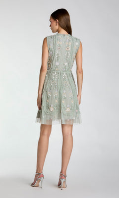 A woman stands with her back to the camera, wearing the Mac Duggal 9135 Embroidered Short Party Dress in light green and high-heeled sandals.