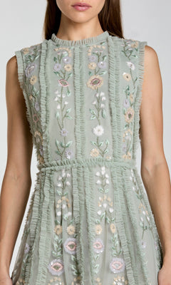 A woman wearing the Mac Duggal 9135, an embroidered short party dress with a sleeveless light green design and vertical ruffle details.