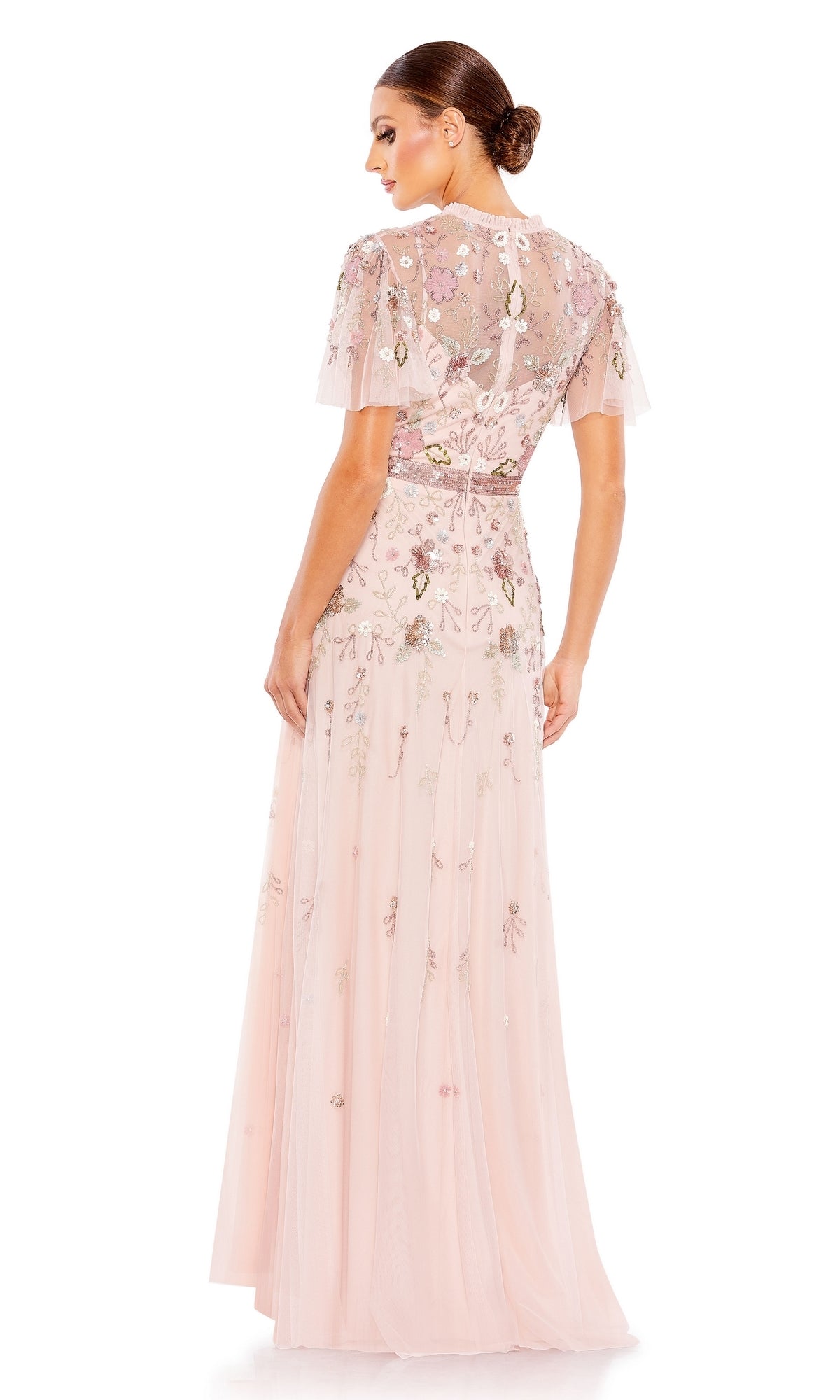 A woman showcases the elegant silhouette and sheer back of the Mac Duggal Long Formal Dress 9136, featuring light pink beaded fabric, short sleeves, and floral embroidery.