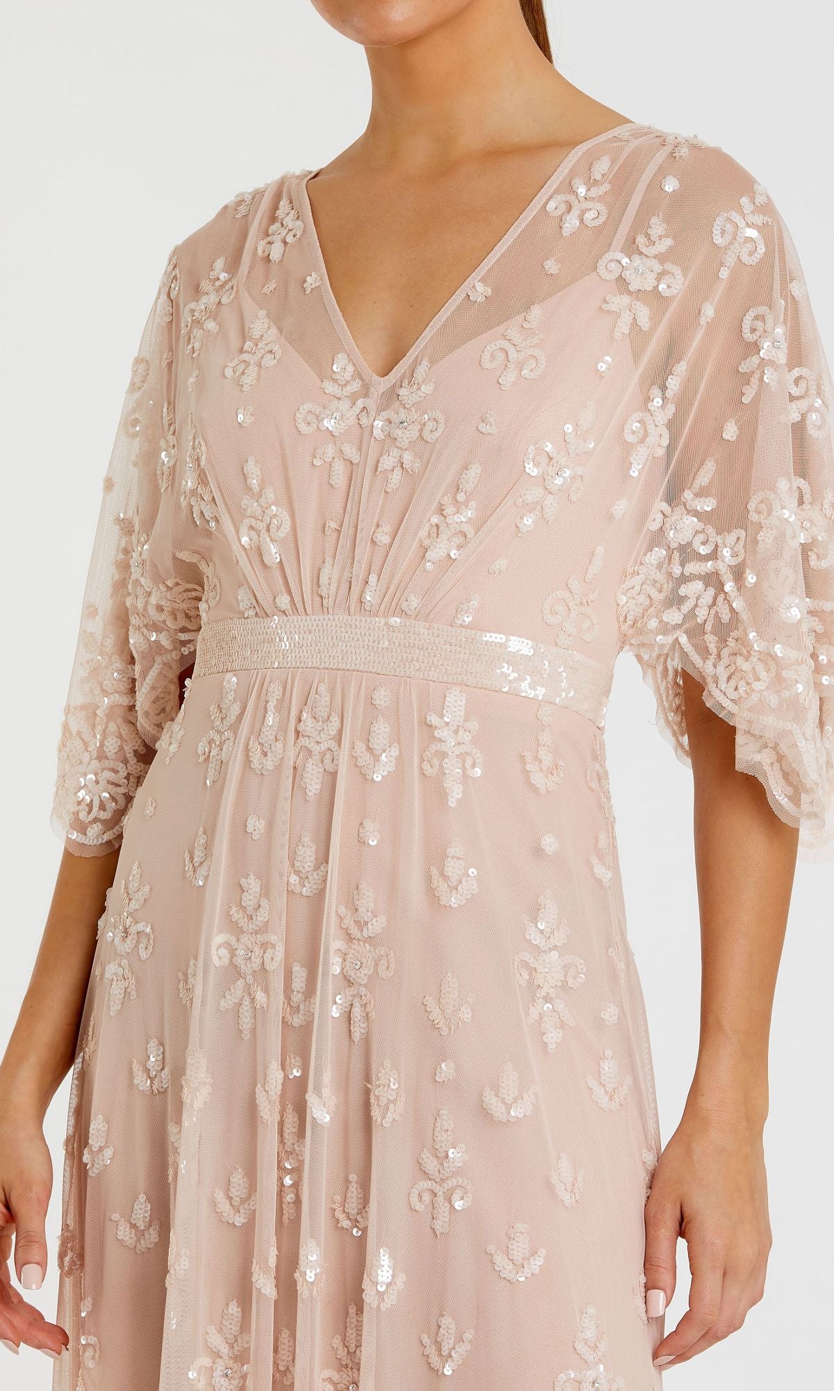 A woman wears the Mac Duggal 9144 Long Pink Sequin Formal Dress, featuring a V-neck, floral sequin embroidery, and sheer flared sleeves.
