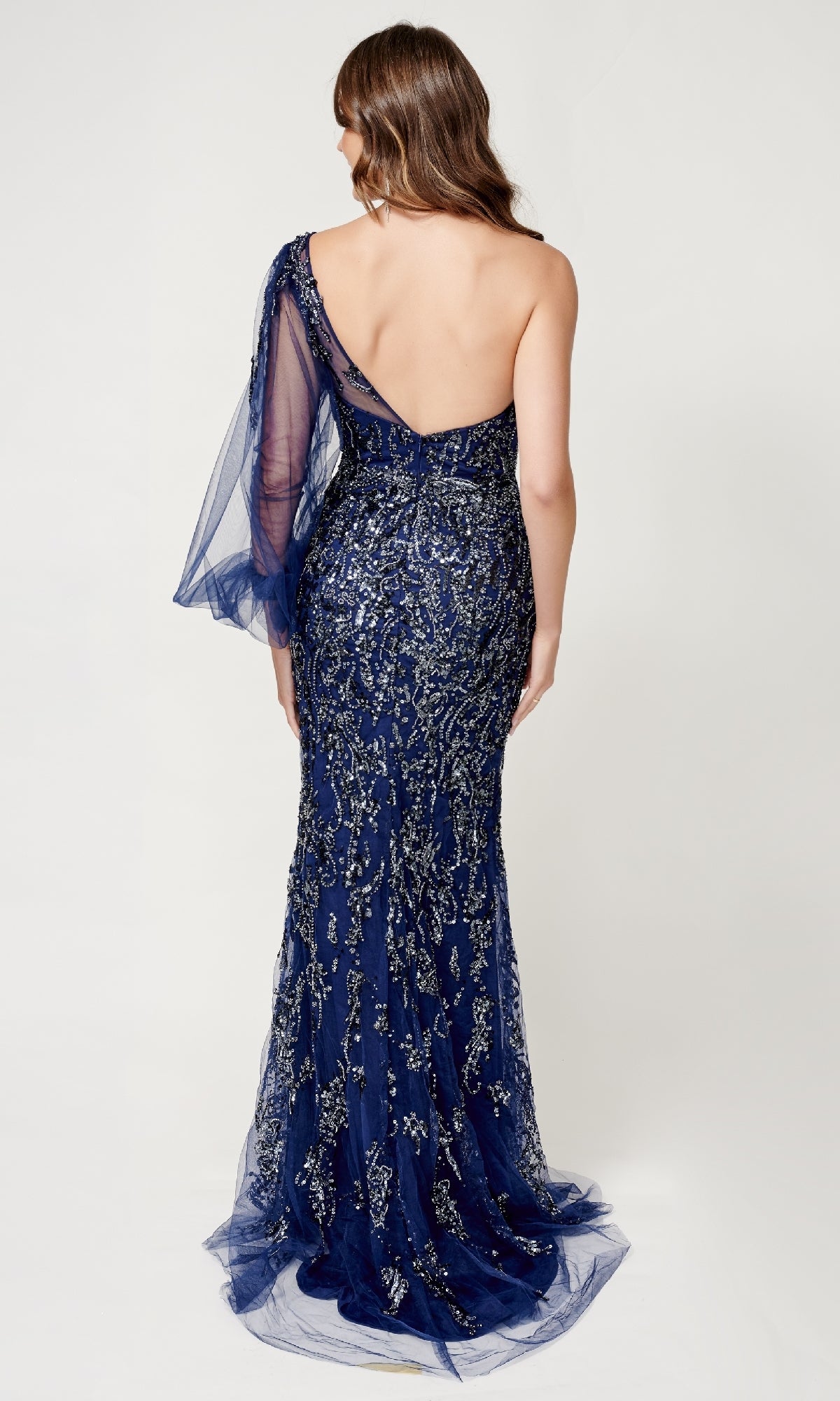 A woman shown from the back wearing the Nina Canacci 9159: a navy blue, floor-length formal dress featuring a one-shoulder neckline, sequin embellishments, and tulle detail.