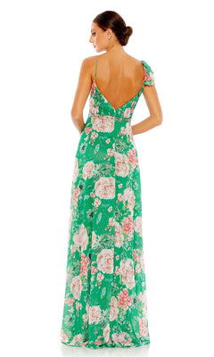 A woman with her hair in a low bun stands facing away, wearing the Mac Duggal 9175 long green print formal dress featuring a floral pattern and a low V-back.
