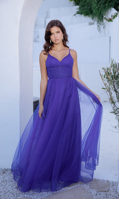 A woman stands outdoors before a white wall, wearing the Corset Long Tulle Prom Ball Gown: Eureka 9177—a sleeveless, floor-length purple dress with a fitted corset bodice and sheer flowing skirt.