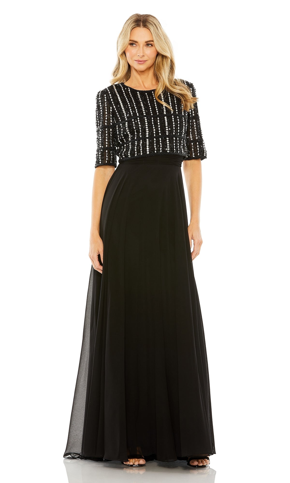 A woman stands facing forward in the Mac Duggal 9180 short sleeve long formal dress featuring a beaded crop top and flowing a-line skirt.