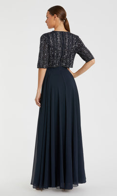 A woman faces away from the camera in the Mac Duggal 9180 short sleeve long formal dress, featuring a navy blue A-line silhouette with a beaded bolero jacket.