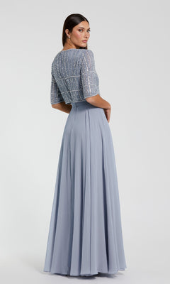 A woman poses with her back slightly turned, wearing the Mac Duggal 9180—an elegant short sleeve long formal dress with a beaded bodice and flowing light blue skirt.