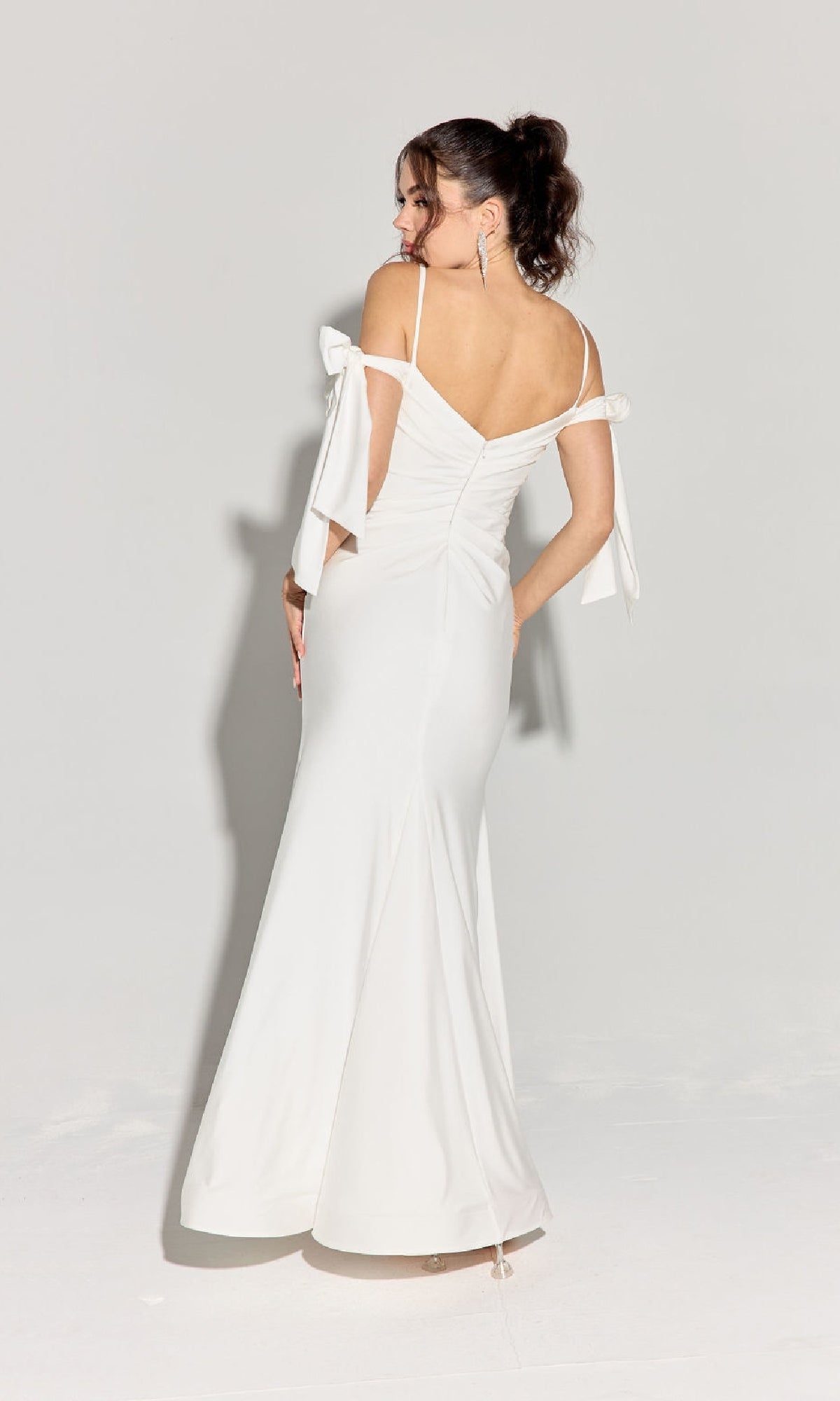 A woman faces away, wearing the Eureka 9181 Shoulder-Ties Long Jersey Prom Dress with bow details and off-shoulder straps, set against a plain light background.