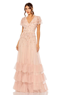 A woman in the Mac Duggal 9189 Short Sleeve Ruffle Formal Dress—light pink, floor-length, with floral embroidery and tiered ruffle layers—stands against a plain white background.