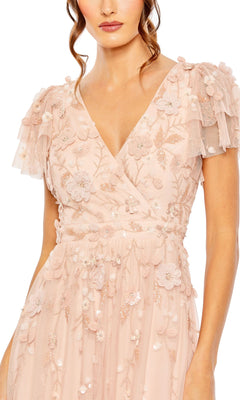 A woman wears the Mac Duggal 9189 Short Sleeve Ruffle Formal Dress in blush pink, featuring a V-neckline, short ruffled sleeves, and elegant floral embroidery.