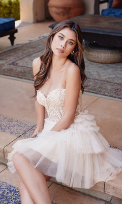 A woman wearing the Embroidered Glitter Homecoming Dress: Juliet JT918S sits on tiled steps beside a patterned rug and outdoor furniture.