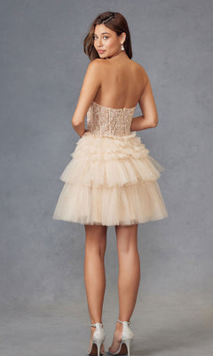 Woman in the Embroidered Glitter Homecoming Dress Juliet JT918S, featuring a strapless sweetheart neckline, lace bodice, and tulle skirt, stands against a gray studio backdrop, facing away but turning to look back in heeled sandals.