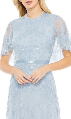 A woman wears the Mac Duggal 9192, a short-sleeve blue formal dress featuring sequin embellishments, a sheer overlay, and delicate floral details.