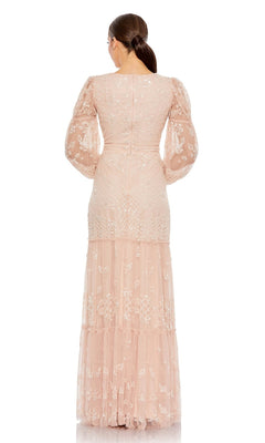 A woman faces away in the Long Formal Dress 9197 by Mac Duggal—a blush pink, floor-length gown with lace details, puffed sheer sleeves, and a tiered skirt. Her hair is styled in a low ponytail against a plain white background.