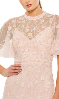 A woman poses confidently with one hand on her hip, wearing the Mac Duggal 9199 Short Sleeve Beaded Formal Gown in light pink, featuring sheer floral lace and pearl embellishments.