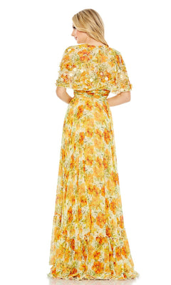 A woman stands facing away, wearing the Long Formal Dress 9201 by Mac Duggal—a floor-length, yellow floral A-line cape dress with short sleeves and a flowing skirt.