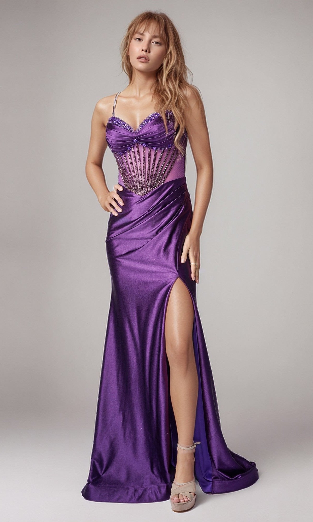 A woman wears the Nina Canacci 9206 long formal dress in plum, featuring a floor-length design with a thigh-high slit, corset-style bodice, spaghetti straps, and lace-up back, paired with platform heels.