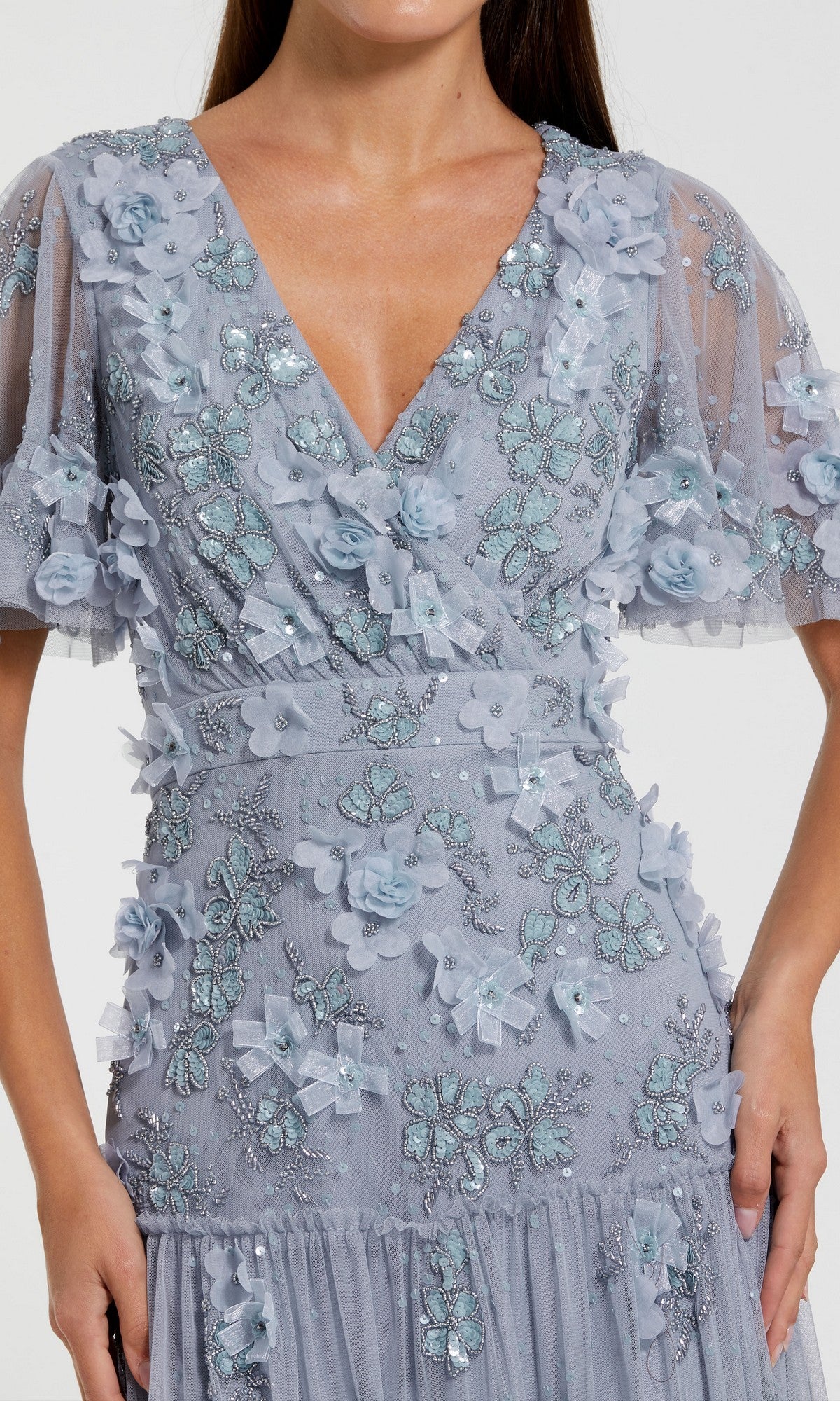 A woman wearing the Mac Duggal 9207 A-Line Wedding Guest Dress, a light blue tea-length gown featuring floral embellishments, embroidered butterfly designs, and short sheer sleeves.