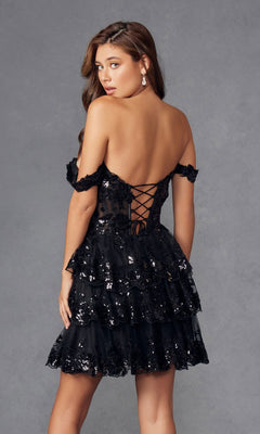 A woman poses against a plain gray background, wearing the Sequin Sheer Corset Homecoming Dress: Juliet JT920K—a short, black off-the-shoulder style with sequins and lace-up back detail.