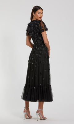 A woman stands facing away from the camera in a Mac Duggal 9212 Floral Midi Wedding-Guest Dress with short sleeves, ruffle hem, and silver high-heeled sandals against a plain background.