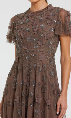 A woman wears the Mac Duggal 9212 Floral Midi Wedding-Guest Dress featuring brown short sleeves, a sheer overlay, floral appliqués, and sequin detailing.