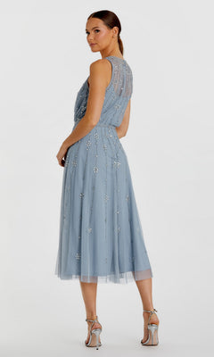 Woman in the Mac Duggal 9222 Midi Wedding Guest Dress—sleeveless, light blue with beaded floral details and a knee-length A-line silhouette—poses against a plain backdrop, paired with silver high-heeled sandals.