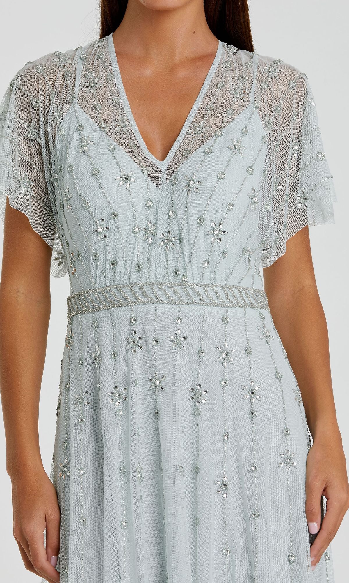 A woman wearing the Mac Duggal 9223 Short Sleeve Long Formal Dress, light blue with sheer sleeves, silver beading, and geometric sequin embellishments.