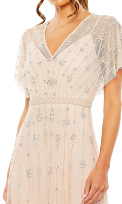 A woman wearing the Mac Duggal 9223 Short Sleeve Long Formal Dress—a light pink sheer evening gown with a V-neckline and floral sequin embellishments.