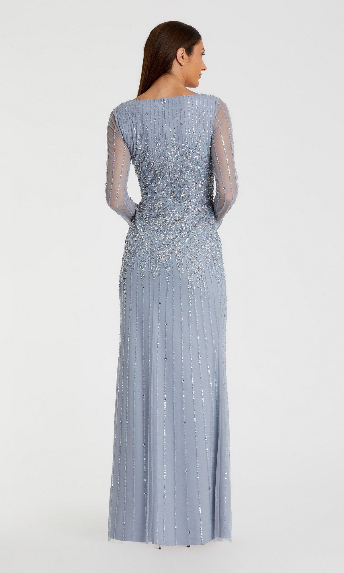 A woman faces away wearing the Mac Duggal 9226 Long Sleeve Sequin Formal Gown—a fitted light blue dress with sheer sleeves and silver sequin embellishments—shown against a plain white background.