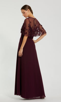 Woman in a floor-length Mac Duggal 9229 Short-Sleeve Long Prom Dress, dark purple with a sheer, embroidered capelet, standing and looking over her shoulder against a plain background.