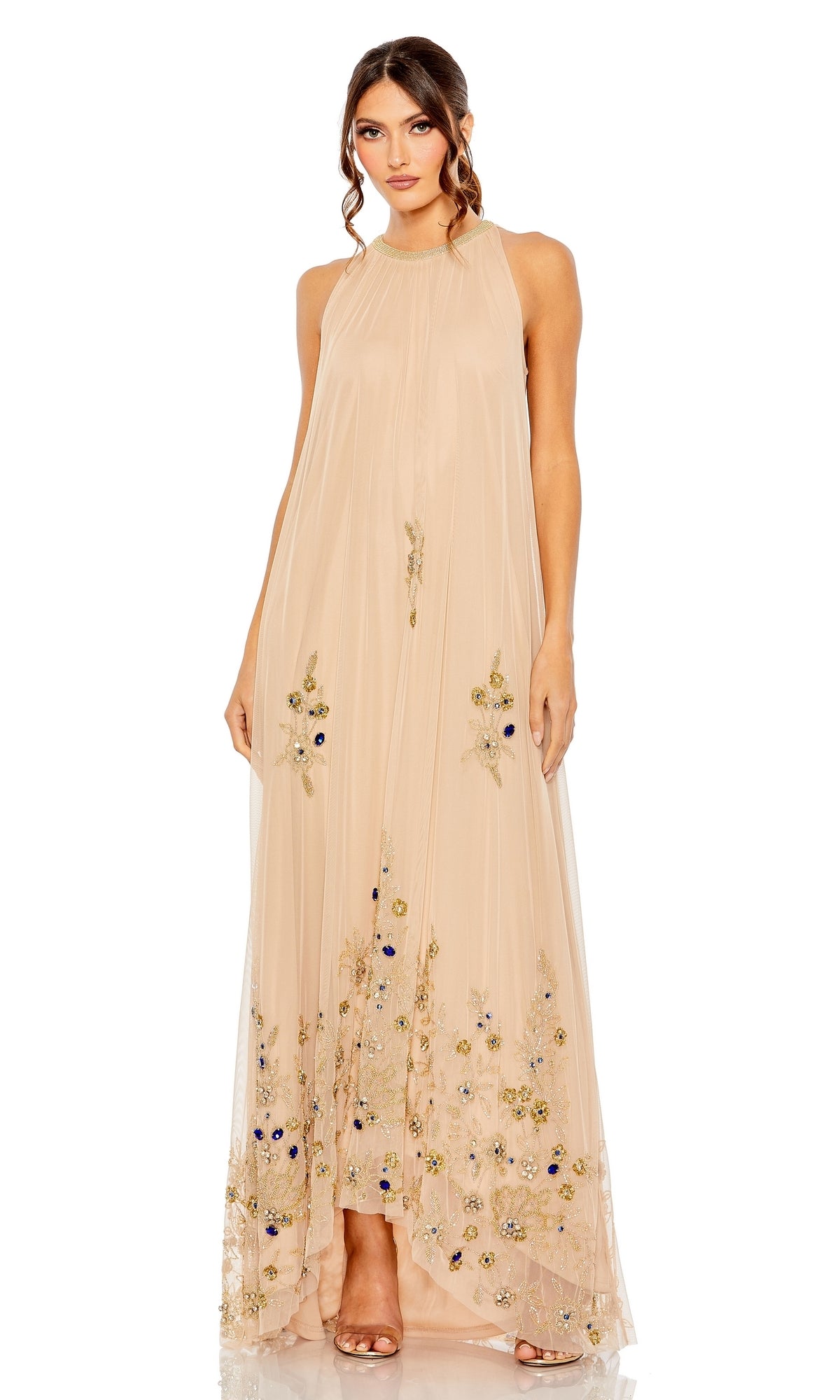 A woman stands wearing the Mac Duggal 9232 Nude Gold Long Trapeze Formal Dress with floral embroidery near the hem, paired with open-toe heels.